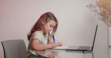 Çalışkan kız, öğretmenle video görüşmesi üzerine alıştırma kitabında yazılan bitirilmiş görevi gösterir. Küçük çocuk evde masa başında internetten eğitim görüyor.