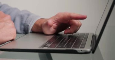 Programmer writes code for website using laptop in office. Hands of man press buttons of keyboard of electronic device on glass desk closeup