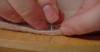 Hands of woman hammer nail into wooden mold through brim of felt hat. Milliner designs shape of headwear for women in workshop extreme closeup