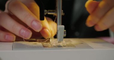Hands of woman put pink thread into tiny needle hole of sewing machine. Milliner prepares equipment for work with hat in workshop extreme closeup