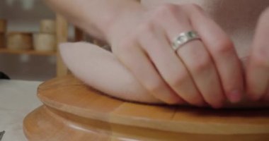 Hands of woman stretch material of felt hat to make brim shape. Milliner finishes working with headwear on round wooden mold in workshop closeup