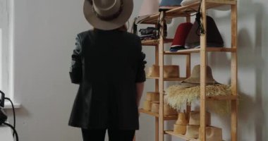 Female milliner takes felt hat blank and puts on table in workshop. Woman prepares glue in glass for spreading on handmade headdress close view
