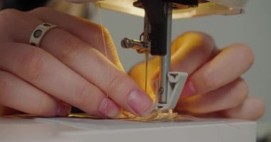 Woman puts pink thread into needle hole of sewing machine on grey background. Milliner prepares equipment for work in workshop extreme closeup
