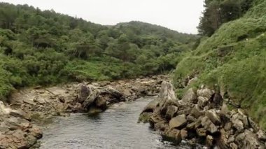 Mountainous narrow river with rapids runs on stone bottom between green hills. Narrow river washes rocky banks under dull sky aerial view