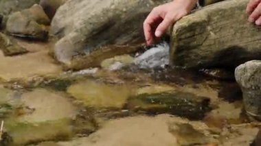 Lady dips hand into clear water with stream flowing through rapids stones. Young woman tourist enjoys wild nature in rural area close view