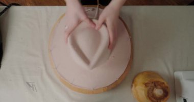 Şapkacı el yapımı başlık tamiri için elleriyle şekil verir. Şapkalı şapkalı şapkalı şapkalı şapkalı şapkalı şapkalı adam masada oturuyor.