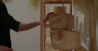 Woman takes wooden molds standing on shelf in workshop to shape hat. Professional milliner prepares equipment for creating headwear closeup
