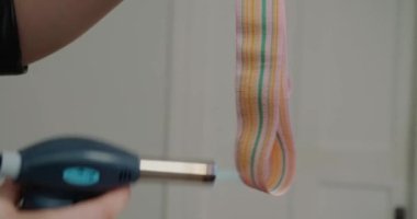 Kadın, arka planında alev püskürtüsü olan geniş renkli bir şapka şeridi işliyor. Şapkacı, el yapımı başlık için dekorasyon hazırlıyor.