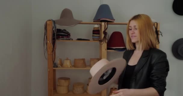 金发女人戴上手工做的带彩带的毛毡帽 转身对着相机 专业的挤压机展示为销售而设计的成品头饰 — 图库视频影像