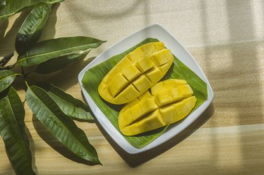 Olgun mangolar tabağa konur ve masaya yapraklar konur..