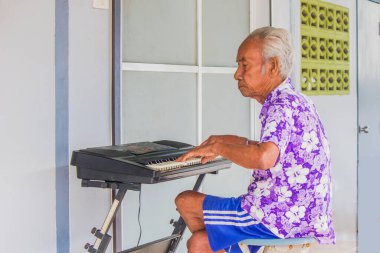 Evin önünde klavye çalan yaşlı bir kişi