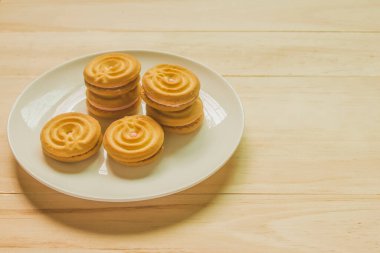 Beyaz bir tabakta çilek kremalı tereyağlı kurabiyeler ahşap zemine serilmiş, mesaj yazmak için yer bırakıyorlar..