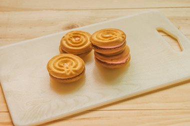 Beyaz kesim tahtasına çilek kreması doldurulmuş tereyağlı kurabiye.