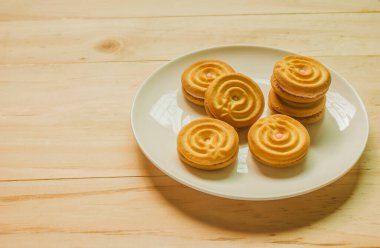 Beyaz bir tabakta çilek kremalı tereyağlı kurabiyeler ahşap zemine serilmiş, mesaj yazmak için yer bırakıyorlar..