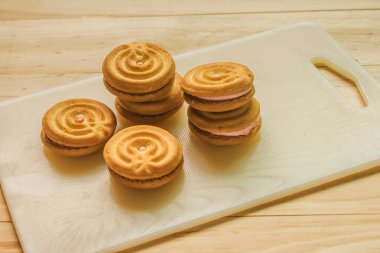 Beyaz kesim tahtasına çilek kreması doldurulmuş tereyağlı kurabiye.