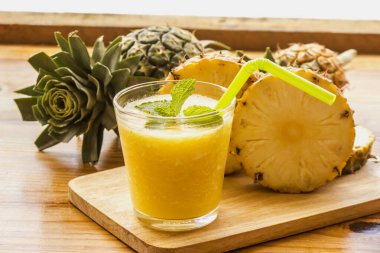 Naneli yaprakların üzerinde ananas ve tahta kesme tahtasının üzerinde dilimlenmiş ananas..