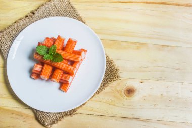 Crab sticks on a white plate with mint leaves on a rustic wooden floor, leaving room for text.
