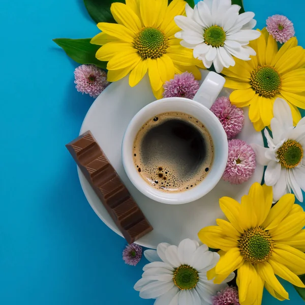 Espresso ile beyaz kahve fincanı, mavi arkaplanda çiçekler ve metin için boş alan.