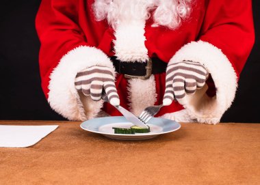 Geleneksel kırmızı kostümlü Noel Baba salatalık yiyor.