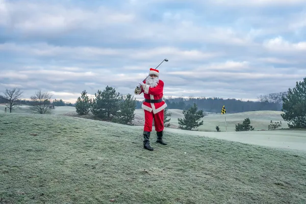 Geleneksel kırmızı kostümlü Noel Baba golf sahasında golf oynar.