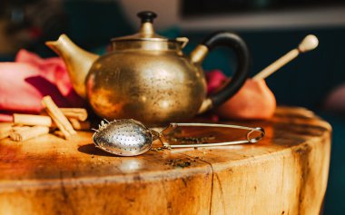 Antika bronz çaydanlık ve sıcak renklerde çay aksesuarlarıyla dolu sağlam bir masa manzarası.