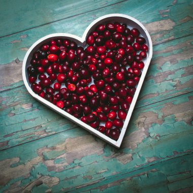 Turkuazın kabataslak arka planında kalp şeklinde kırmızı yaban mersinli kompozisyon.