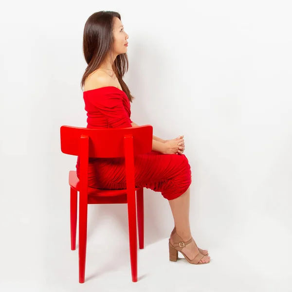 赤いドレスを着たアジア系の女性が赤い椅子の上に腰を下ろして — ストック写真