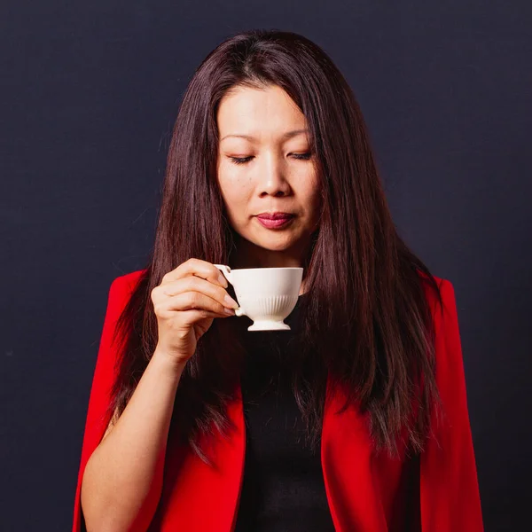 エレガントな赤いジャケットのコーヒーを飲むの長い髪を持つ美しいアジアのビジネス女性 黒い背景で撮影されたスタジオ — ストック写真