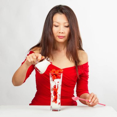 Kırmızı elbise giyen Asyalı kadın lezzetli çilek meyveli tatlı yiyor. Beyaz arkaplanda kırmızı, ön görünüm.