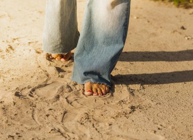 Deniz kıyısının güneşli kumlarında iki kadın ayağının ön görüntüsü. Pembe pedikürlü tırnaklar..