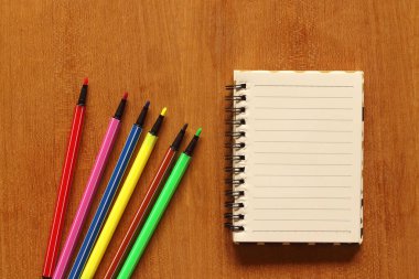 defter ve çok renkli kalemler ahşap masada.