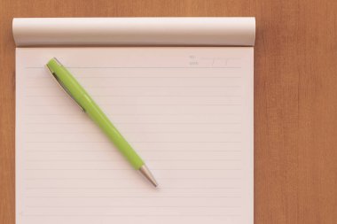 Top view of office desk with open spiral notebook, pen a green on wood table