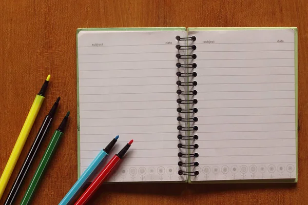 notebook and multicolored pens on wooden table