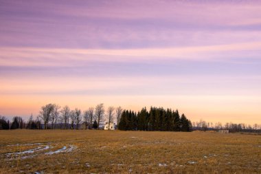 Kış sahnesinde kar ve uzak binalarla dolu bir arazi. 