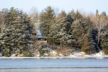 Kış sahnesinde göl ve uzak ev