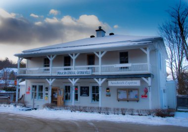 Mavi bulutlu gökyüzünün altında karlı bir sahnede depo binası