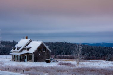 Tahta ev, ağaçlar ve günbatımı gökyüzü olan kış manzarası