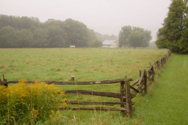 Yeşil tarlada çitlerle çevrili bir çiftlik evi.
