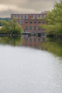 Sakin nehir kıyısında terk edilmiş bir bina. Etrafı ağaçlarla çevrili.