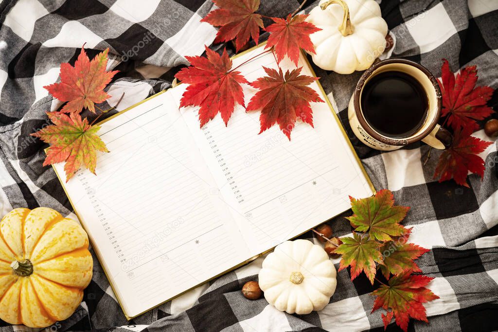 A mug of coffee, mini pumpkins, hazelnuts, red maple leaves and open notebook on a plaid blanket. Autumn flat lay.