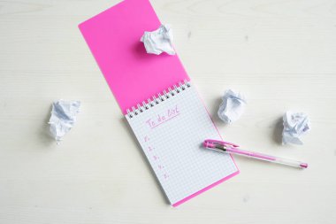 Pembe defter ve kalem kırışık çarşaflı beyaz bir masanın üzerinde. Yapılacaklar listesi.