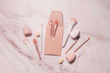 Makyaj sanatçısının mermer bir tuvalet masasındaki pembe aletleri: toz, allık, kaşlar, gölgeler ve kapatıcı ve temel için süngerler.