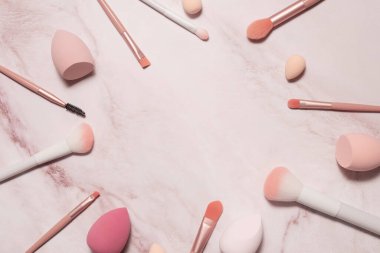 Pembe mermer arka planda kozmetik fırça ve süngerlerin yuvarlak çerçevesi.