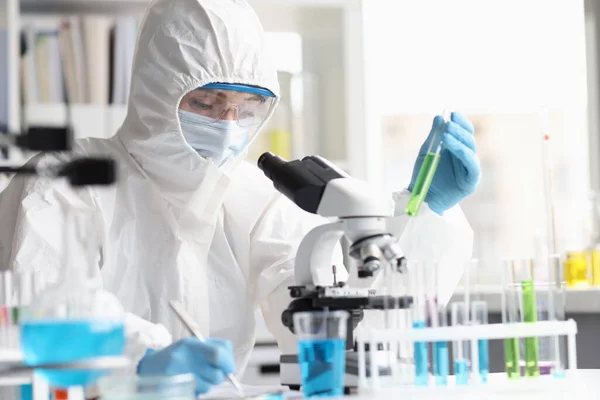 Mulher química em terno protetor realiza pesquisa laboratorial em líquido verde — Fotografia de Stock