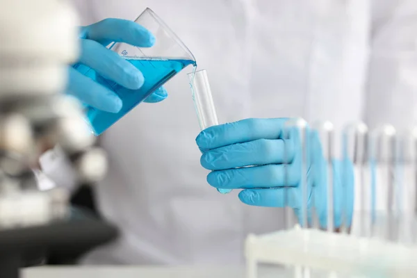 Cientista com luvas derrama líquido azul em tubo de ensaio em laboratório — Fotografia de Stock