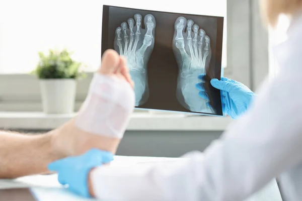 Lékař provádí fyzikální vyšetření pacienta s obvázanou nohou a vyšetřuje rentgenový snímek — Stock fotografie