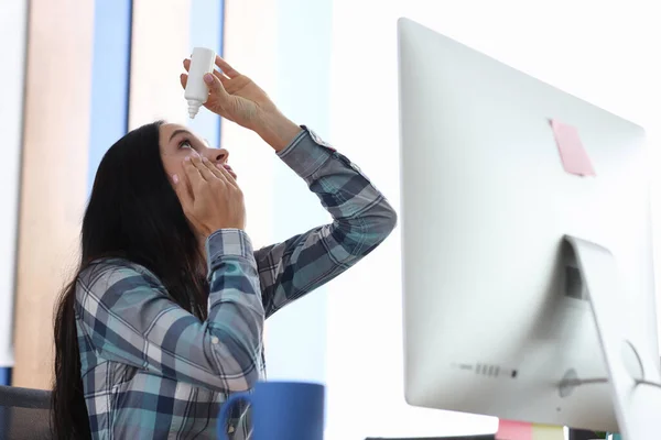 Mujer gotea gotas en los ojos mientras está sentado en el lugar de trabajo en la computadora —  Fotos de Stock