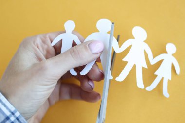 Kadın, kağıt figürlerini makasla yakın plan aile şeklinde kesiyor.