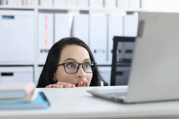 Shocked young woman looks from under table at laptop monitor closeup — Stock Photo, Image