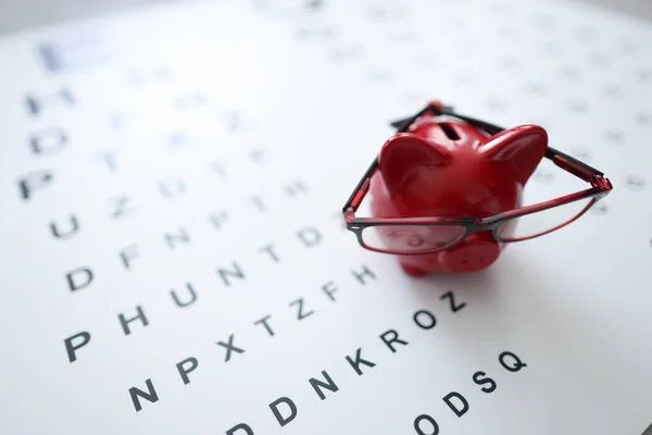 Красная свинья копилка в очках стоит на офтальмологическом столе крупным планом — стоковое фото